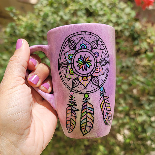 A Pastel Pink hand painted mug with a dreamcatcher in black and colored in with (pink, yellow, purple blue, green and orange)