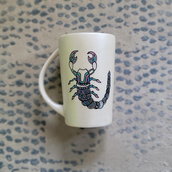 A Pearl white Hand painted Mug With a Scorpio Design on it in Black and colored in pinks, greens and blues