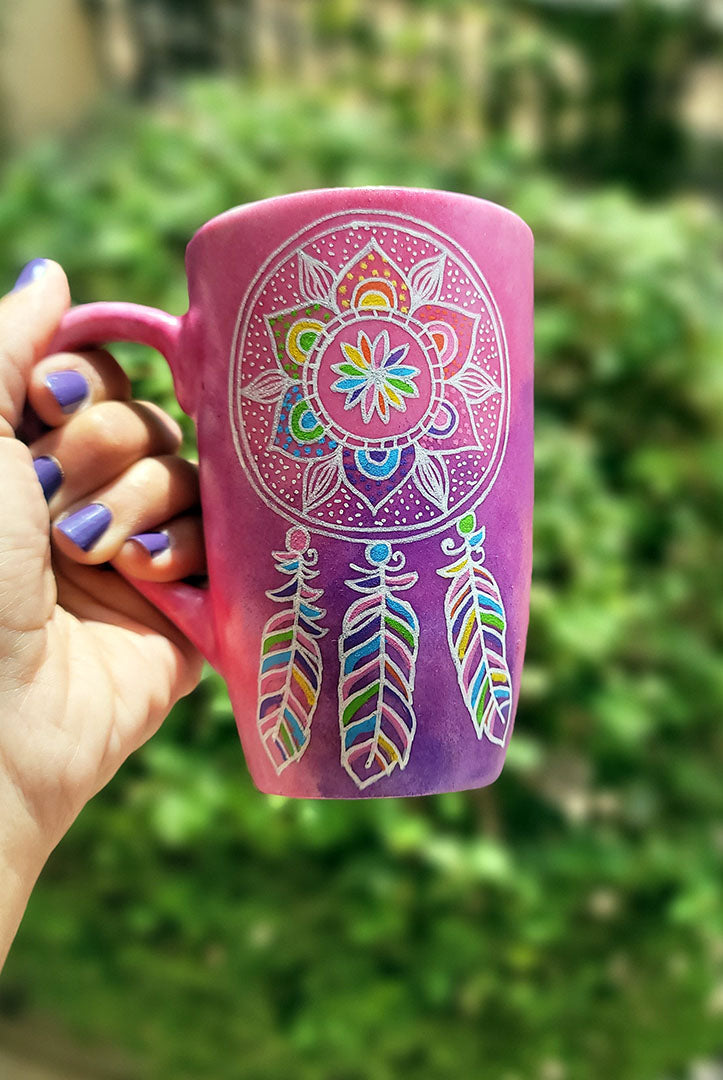 A Pink hand painted mug with a dreamcatcher in white and colored in with (pink, yellow, purple blue, green and orange)