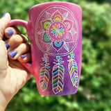 A Pink hand painted mug with a dreamcatcher in white and colored in with (pink, yellow, purple blue, green and orange)