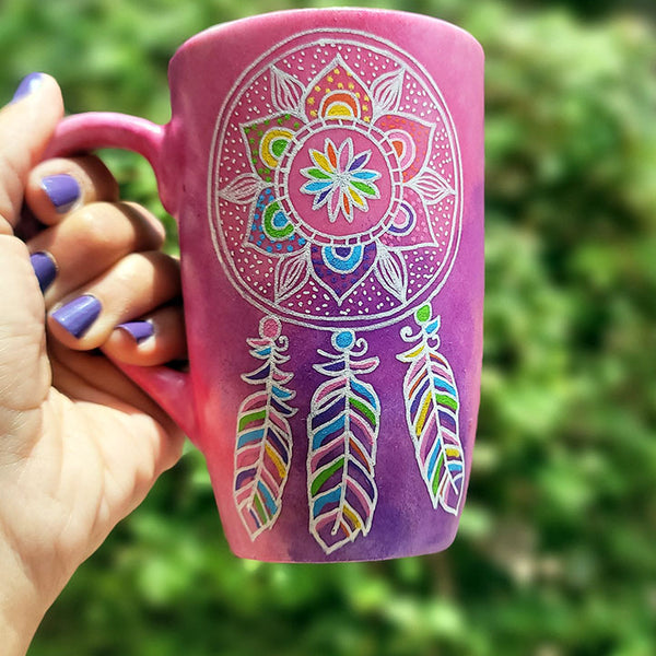 A Pink hand painted mug with a dreamcatcher in white and colored in with (pink, yellow, purple blue, green and orange)