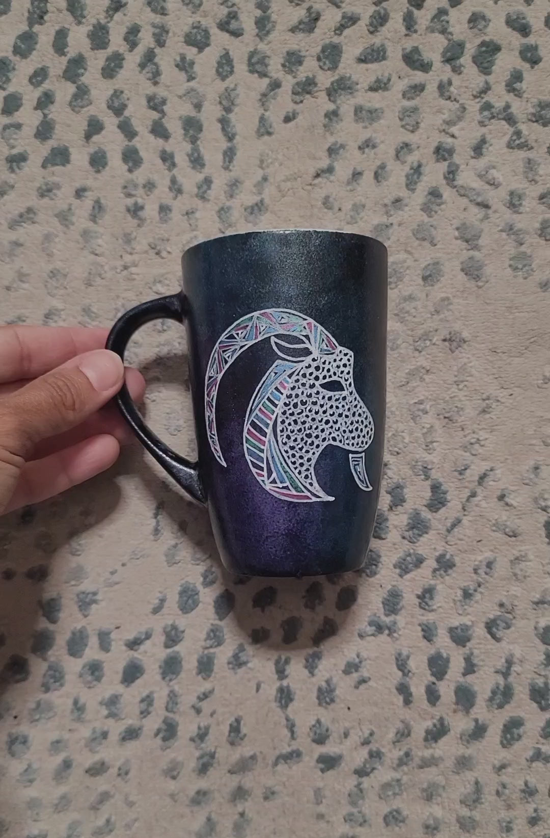 A Video showing a hand-painted  dark galactic colored mug with capricorn on one side and the words "believe in yourself" on the other