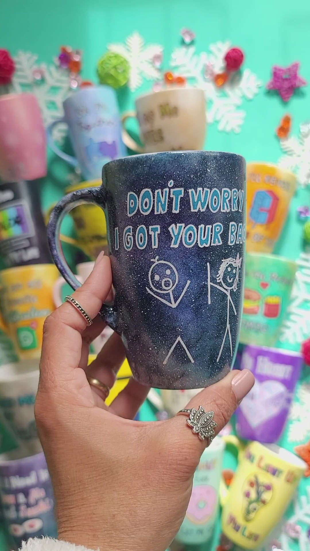 A hand painted black galaxy mug with the words "don't worry, I got your back " and a drawing of 2 stick figures with the girl holding the back of the boy and the name Ingy on the other side