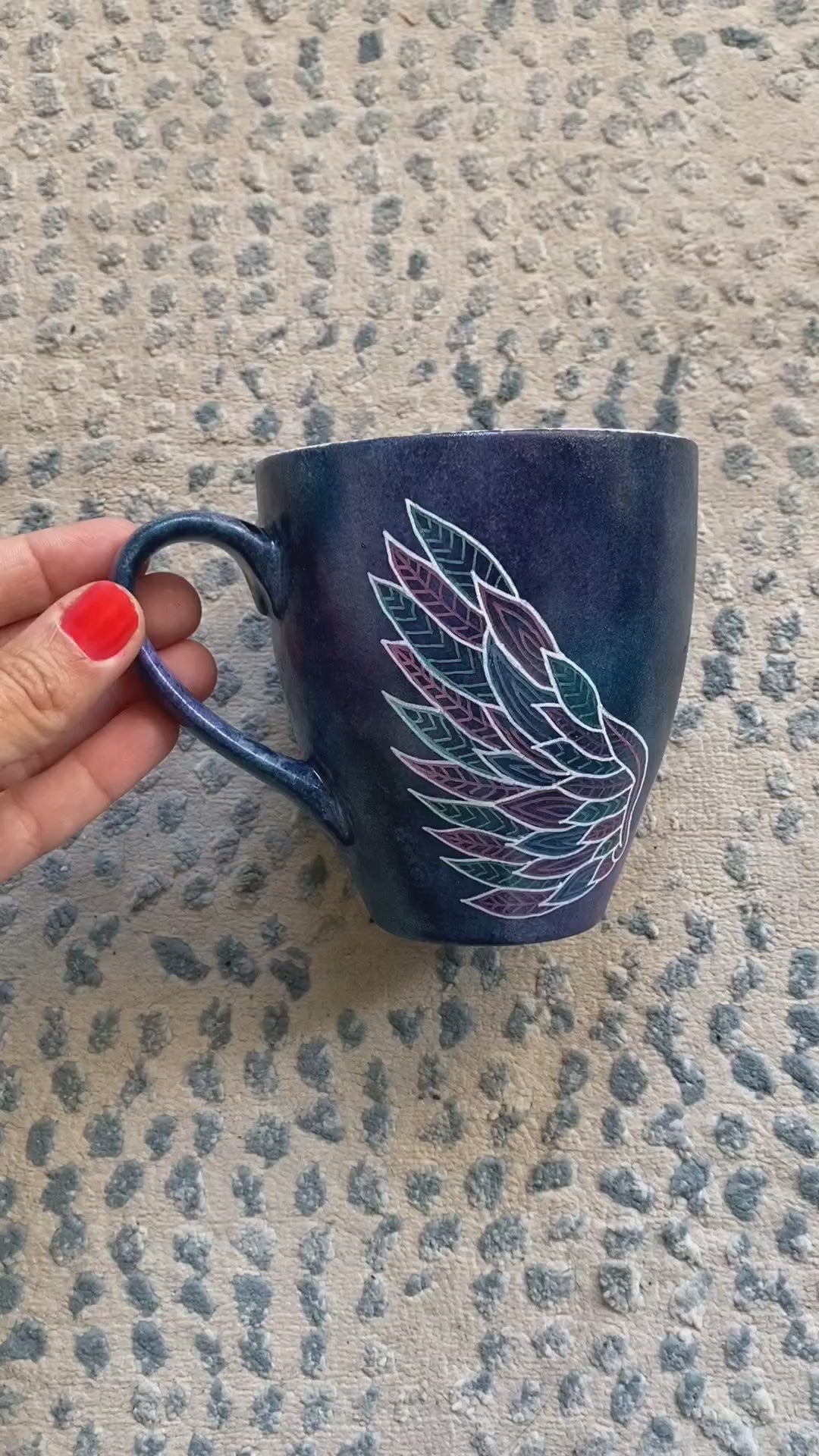 A black galaxy hand painted mug with a wing drawn on one side and the name "Engie" in the center and another wing on the other side