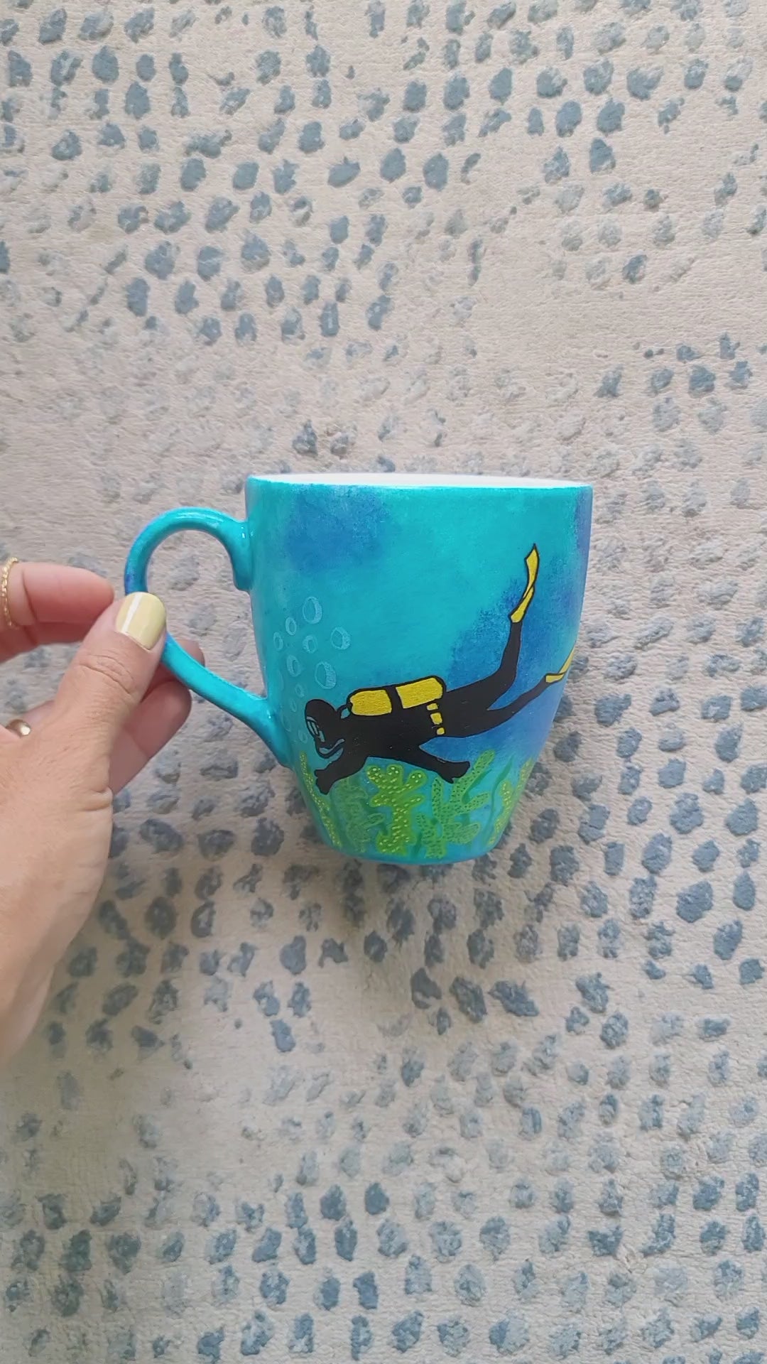 A Blue hand painted mug with a diver painted on it and corals all over the bottom half of the mug and the other side has the name "Zohdy"