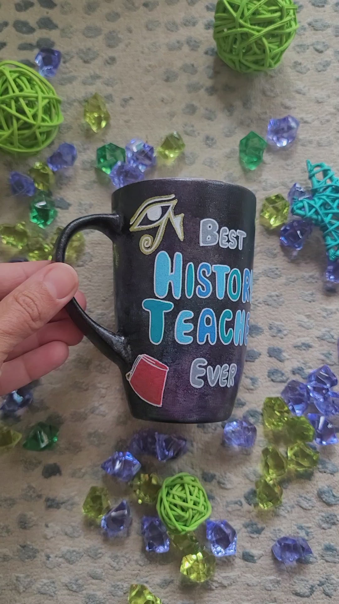 A Black Sky Hand painted mug with the words "Best History teacher Ever" and Egyptian history icons scattered all over and the other side has the name "Mahmod"