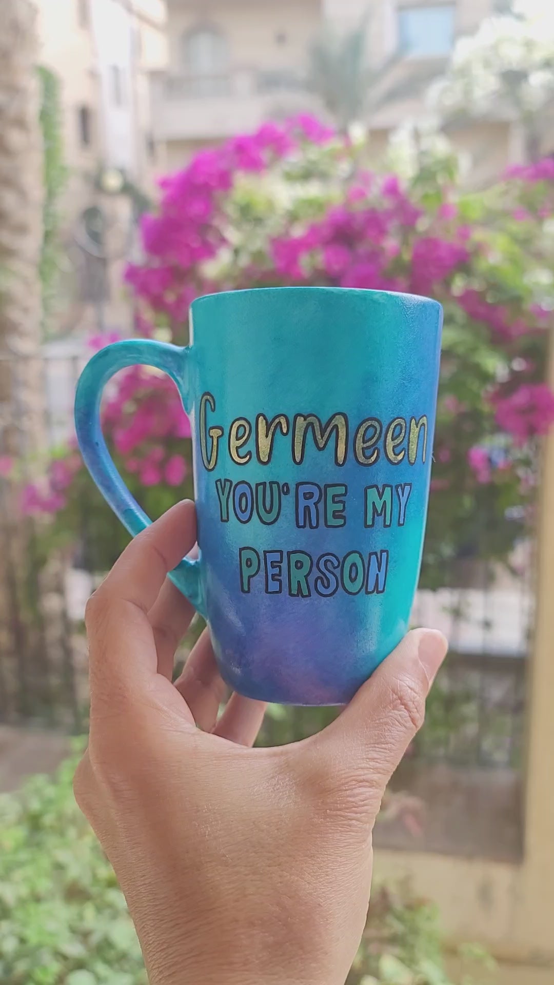 A Hand painted blue mug with the words "Germeen, you're my person". and on the other side an eye painted in the center with gold eye lashes