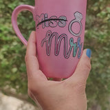 A shimmery pink hand-painted mug with the word miss crossed out and the words mrs in larger font, with a diamond ring drawn on the side. and on the other side the name 