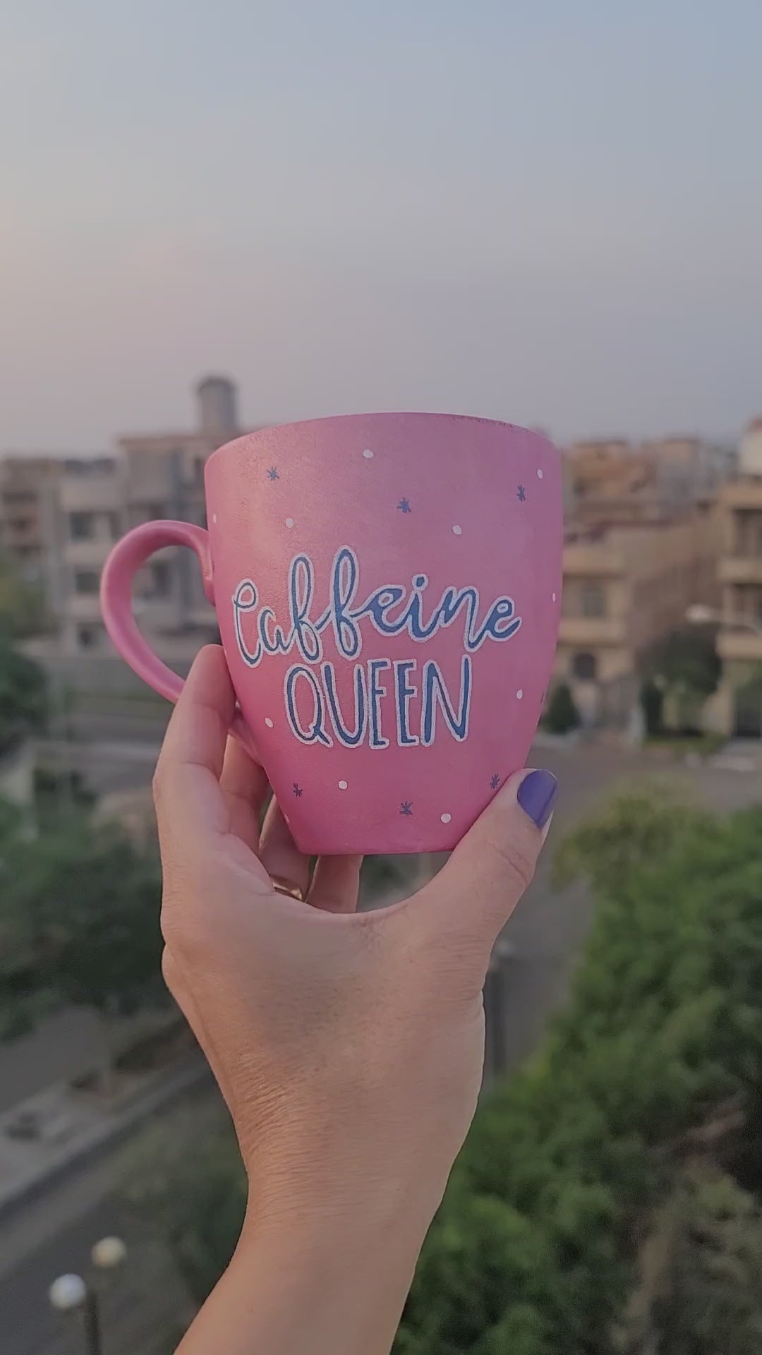 A Hand - painted shimmery pink mug with the words "Caffeine Queen" in blue and the other side has a crown