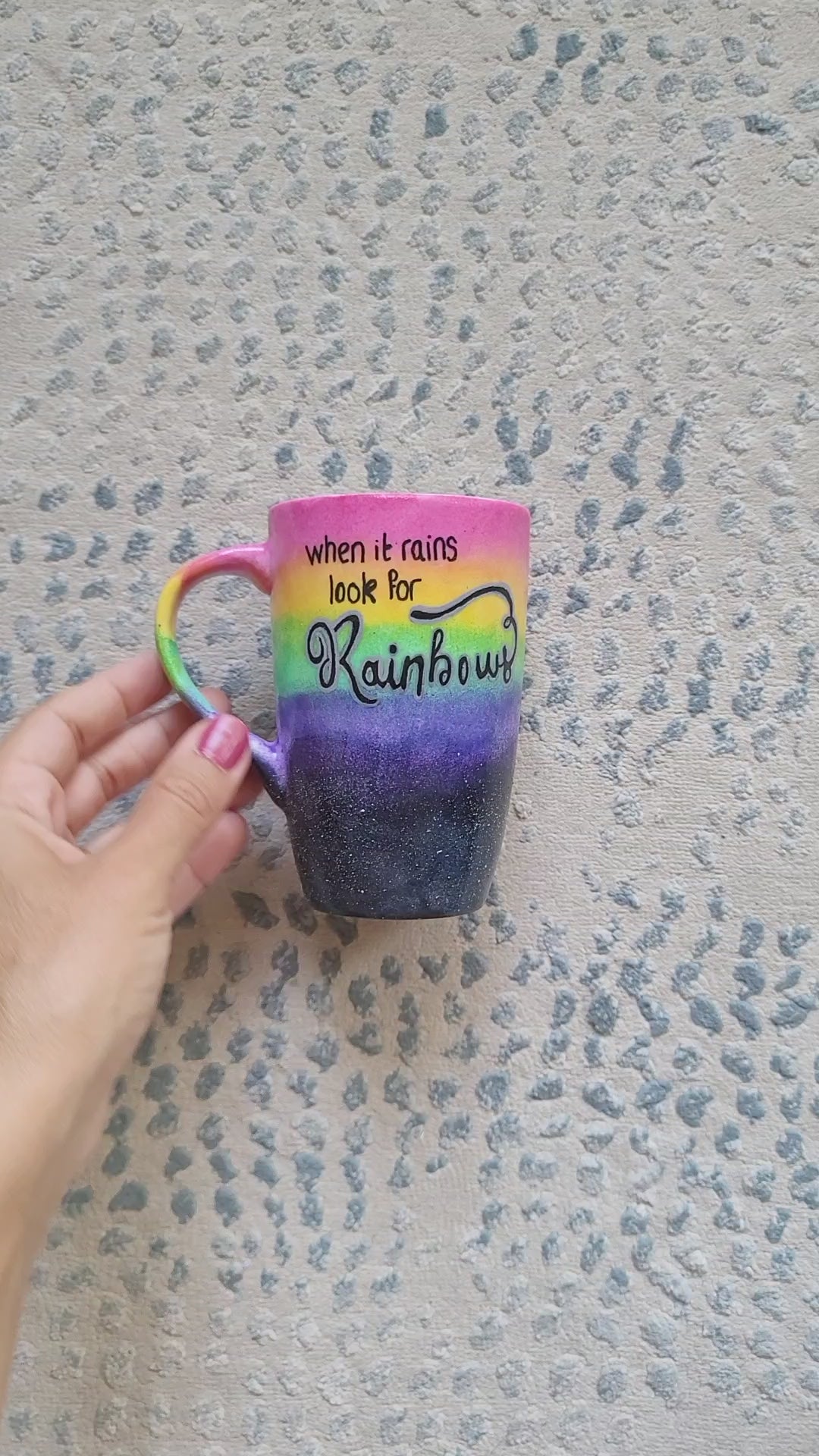 A Mug with the top half painted in rainbow and the bottom in dark galaxy, with the words on the rainbow written "when it rains look for rainbows" and the other side on the dark galaxy the words "when its dark look for stars"