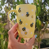 A Pastel yellow Hand painted mug with bees , white flowers and honey combs scattered all over