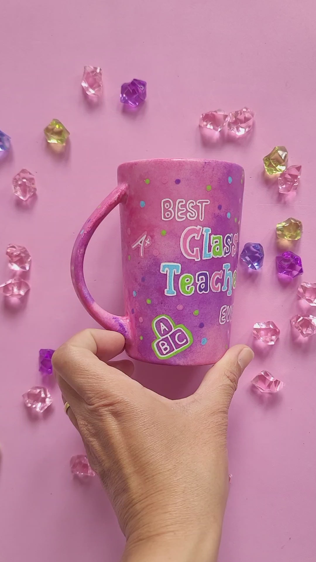 A Pink Hand painted Mug with the words "Best Class Teacher Ever" and school items scattered all over and the other side has the name Chrystal