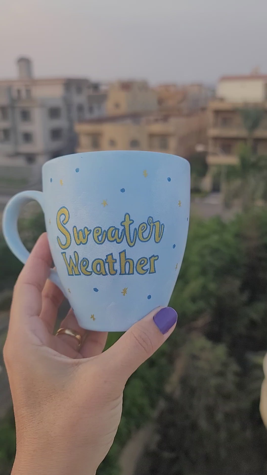 A baby blue hand painted mug with the sentence "Sweater Weather" in gold and on the other side a snowflake