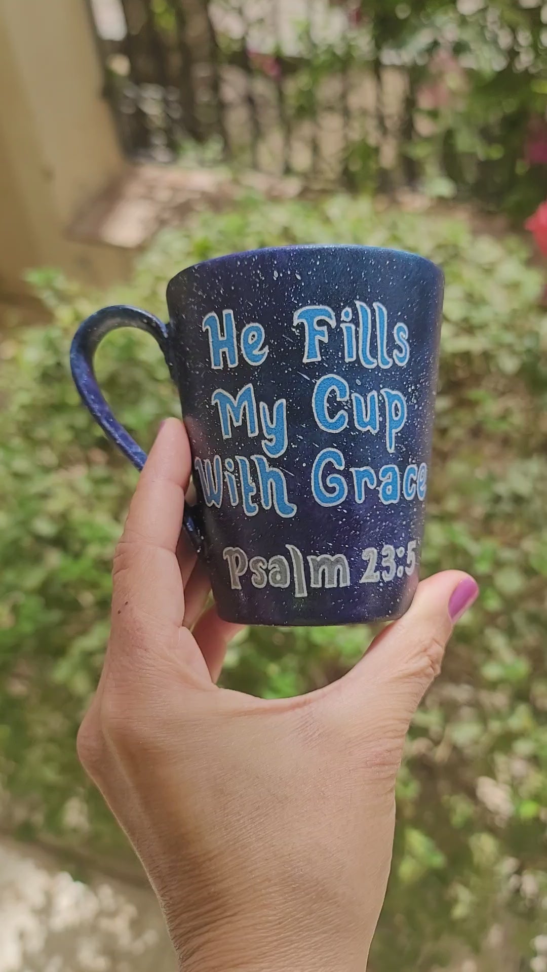 a Bluish galaxy hand painted mug with the words "He fills my cup with grace" Pslam 23:5 and the other side has the name "Mina"