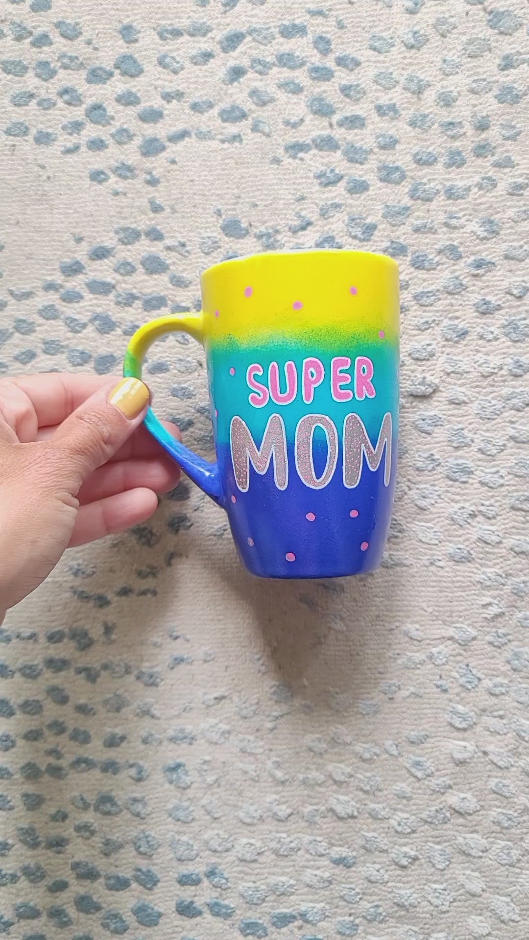 A Gradient colored mug (Yellow blue and ultramarine) with the words "Super Mom" with pink dots scattered all over and the other side has the name "GiGi"