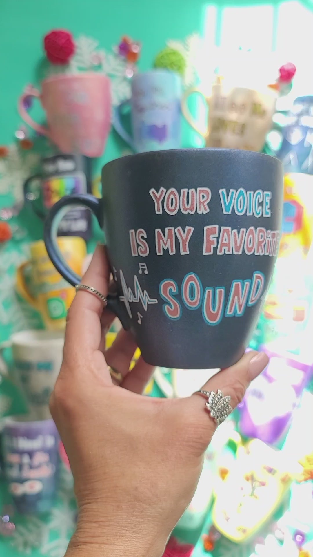 A shimmery blue hand painted mug with the sentence " your voice is my favorite sound" and sound beats painted on both sides and the name "Ayman" on the other side