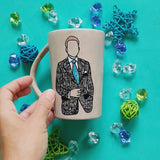 A taupe hand painted mug with a silhouette of a man in a suit filled with patterns and the other side has the words 