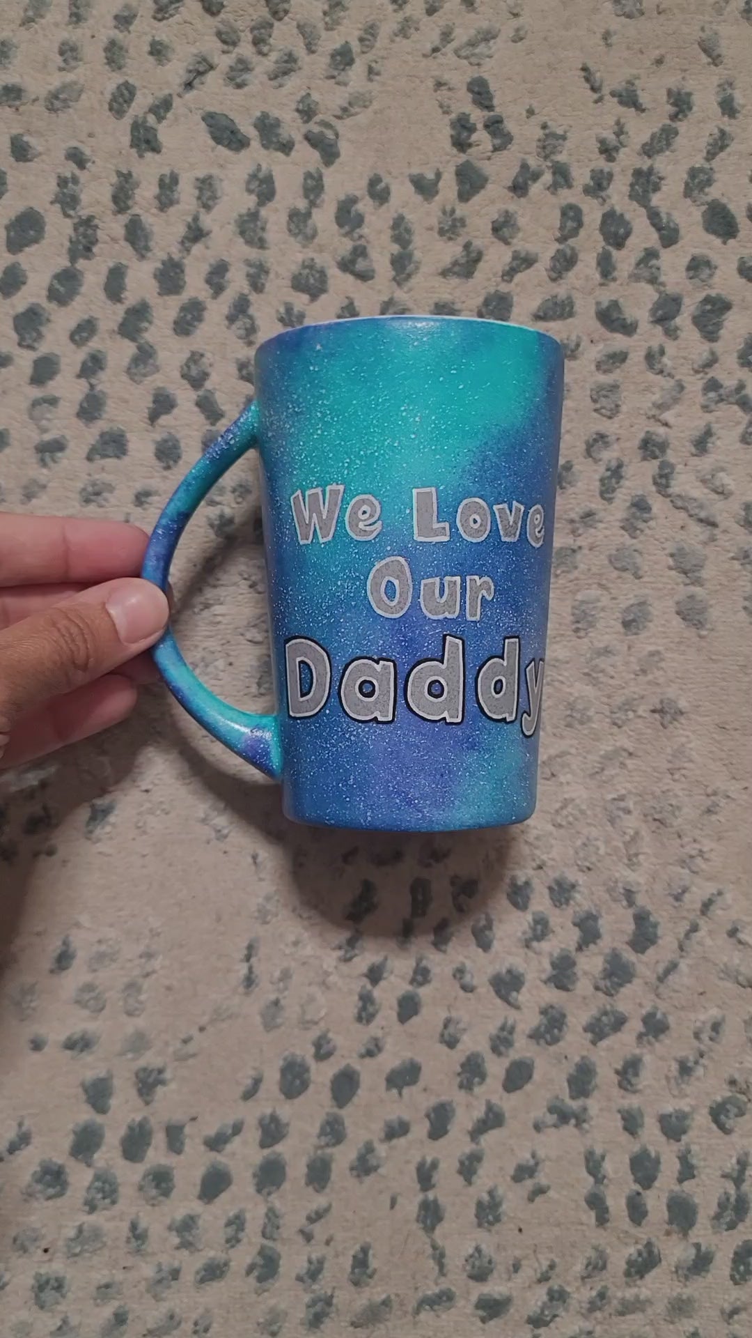 A blue Galaxy hand Painted mug with the sentence "We love our Daddy" and the name "Hossam" on the other side