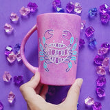 A video showing a hand-painted pink galaxy mug having a cancer sign drawn on one side and the words 