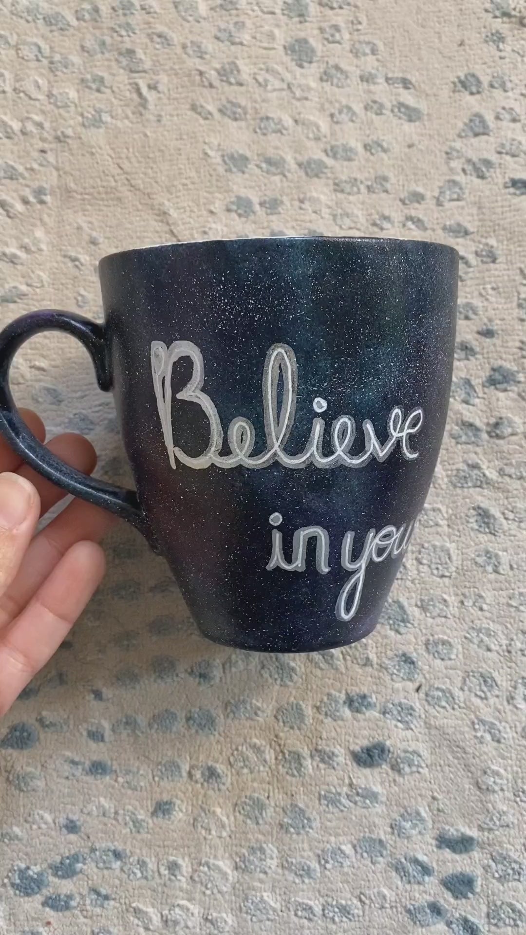 A Black galaxy hand painted mug with the words "Believe in yourself" and the other side has the name "Eman"