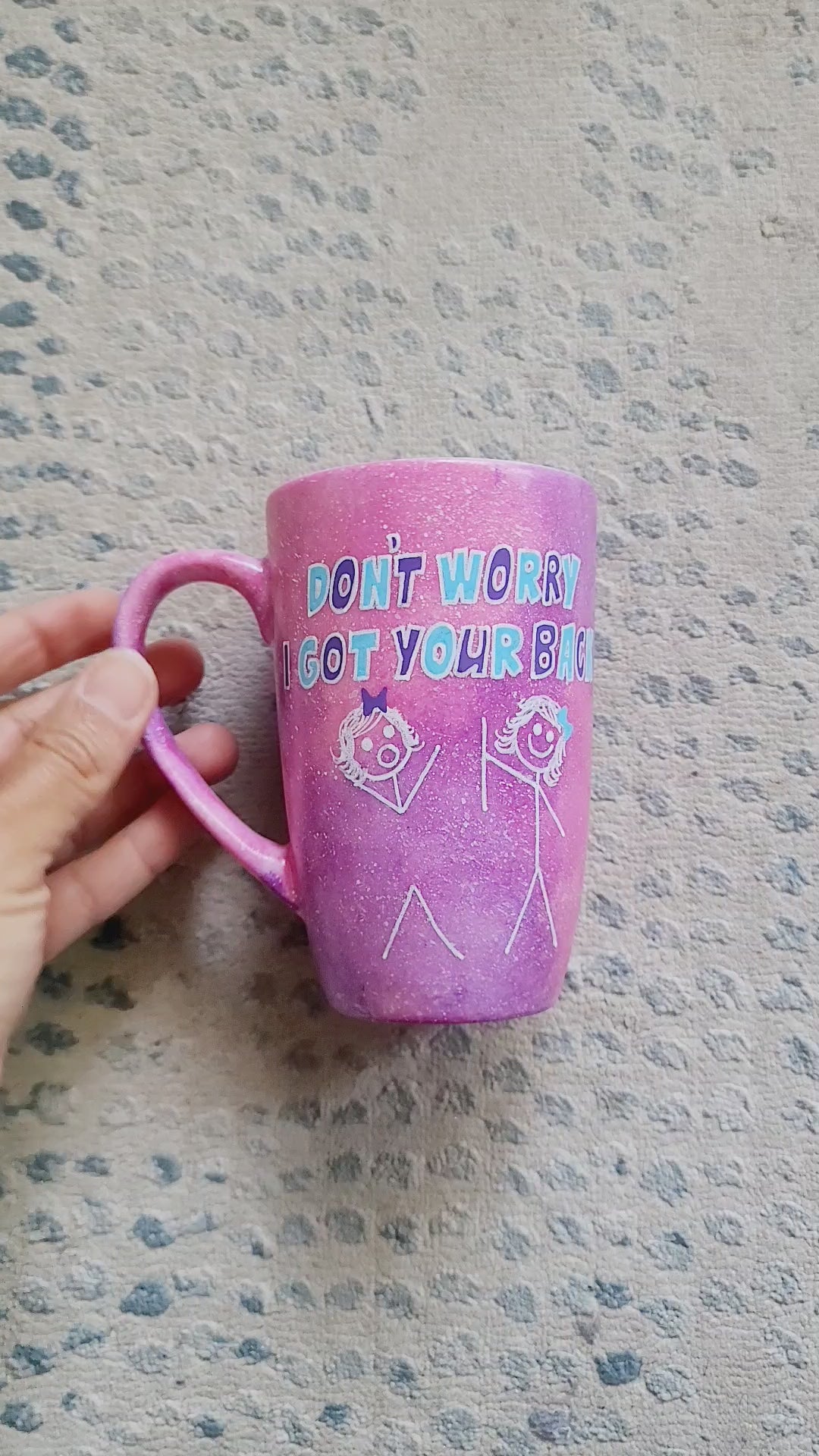 A hand painted pink galaxy mug with the words "don't worry, I got your back " and a drawing of 2 stick figures with the girl holding the back of the other girl on one side and the other has the name "Marmar"