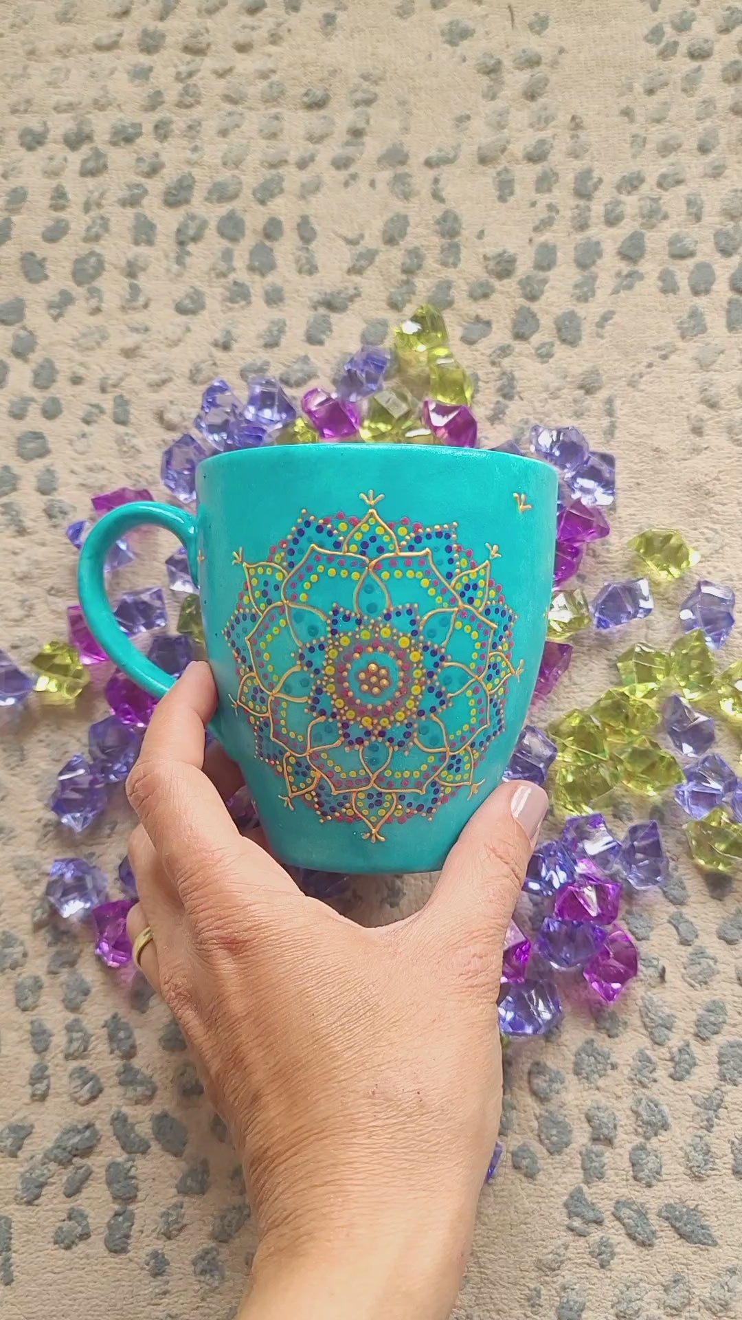 A hand painted blue Indian color mug with a mandala painted in gold and on the other side the words "World's Best Mom " and the name Amal under it in purple