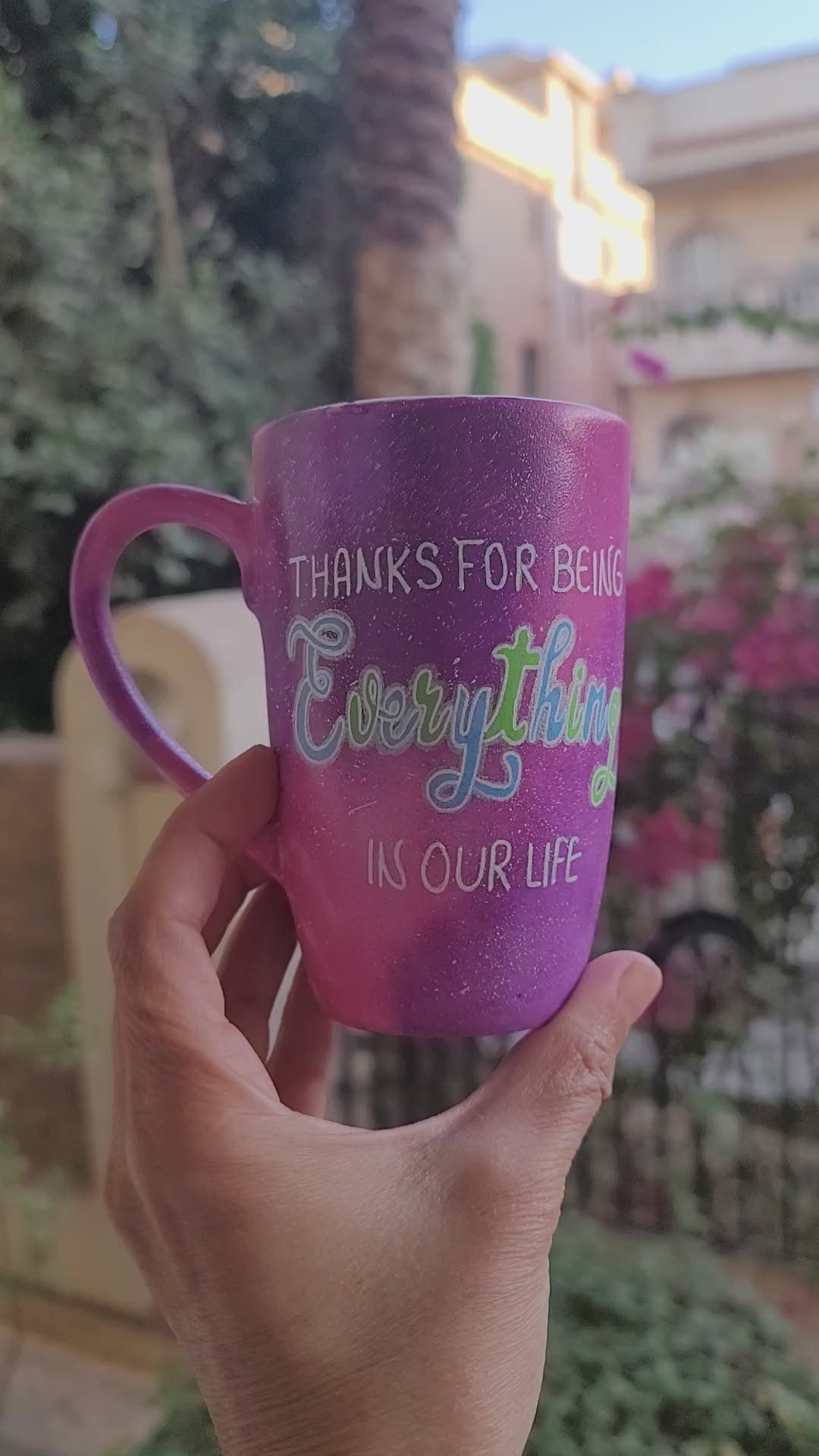 A hand painted pink galaxy mug with the sentence "thanks for being everything in our life" and the name "Nora" on the other side