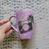 a pastel pink hand painted mug with a camera drawn on it with patterns inside and flowers coming out of its side