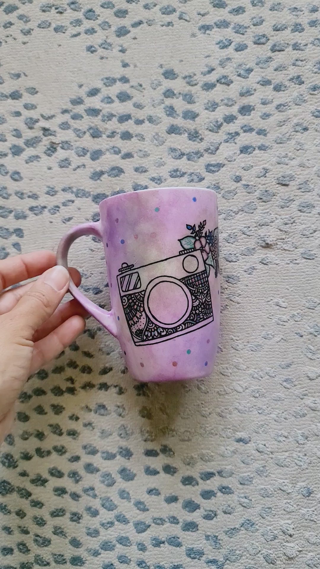 a pastel pink hand painted mug with a camera drawn on it with patterns inside and flowers coming out of its side