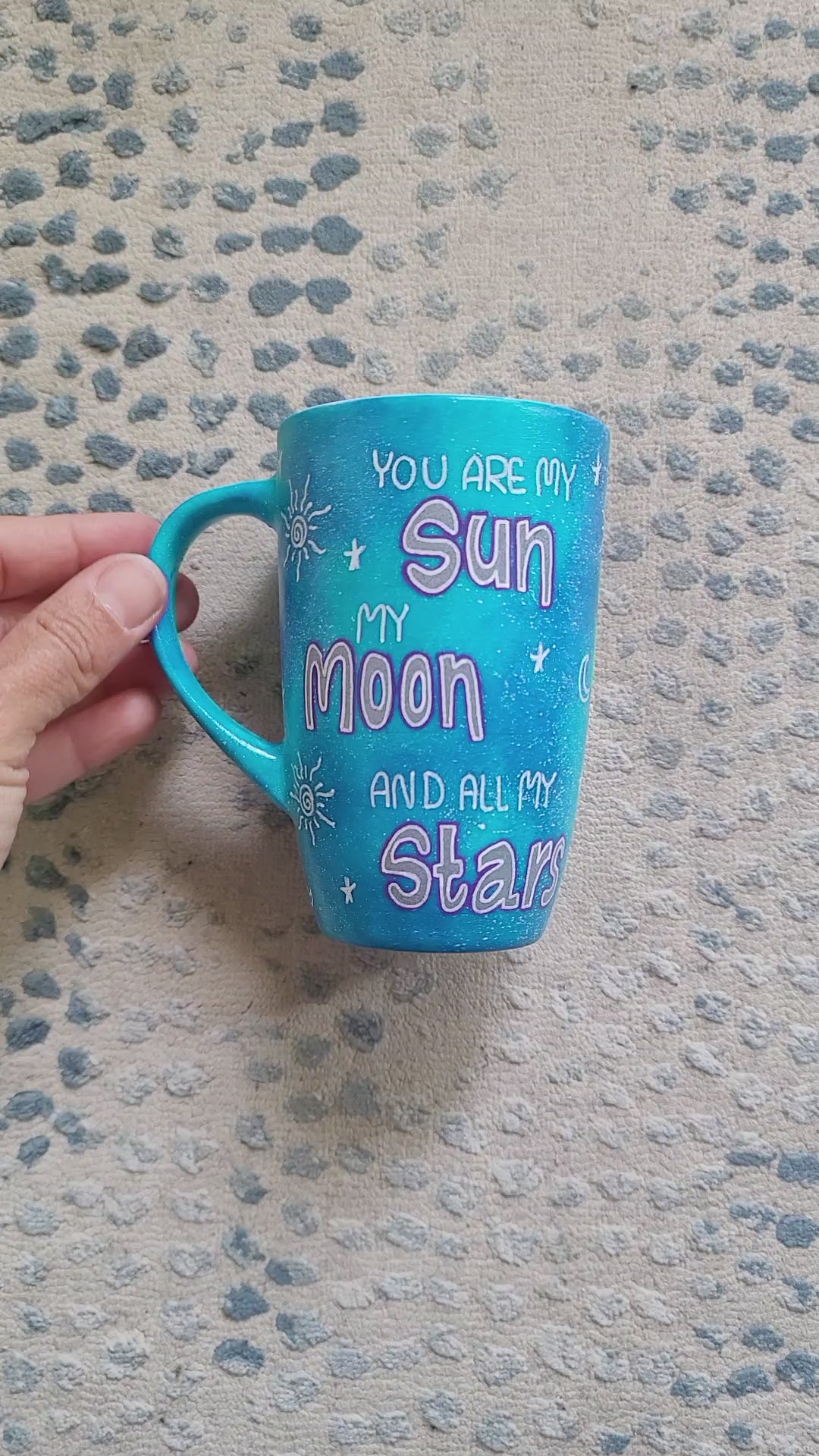 A Blue Galaxy Hand painted mug with the sentence 'you are my Sun, My Moon and all my stars". and on the other side the name "Peter" with small moons stars and suns scattered all over the mug