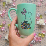 A Mint Hand Painted mug with a bunny drawn on it in black looking up and the bunny itself  has patterns on the corner inside it. and the other side has the sentence 