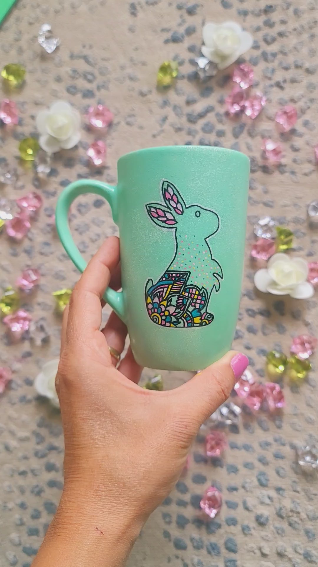 A Mint Hand Painted mug with a bunny drawn on it in black looking up and the bunny itself  has patterns on the corner inside it. and the other side has the sentence "it's more difficult to stay on top than to get there, but I made both look really easy