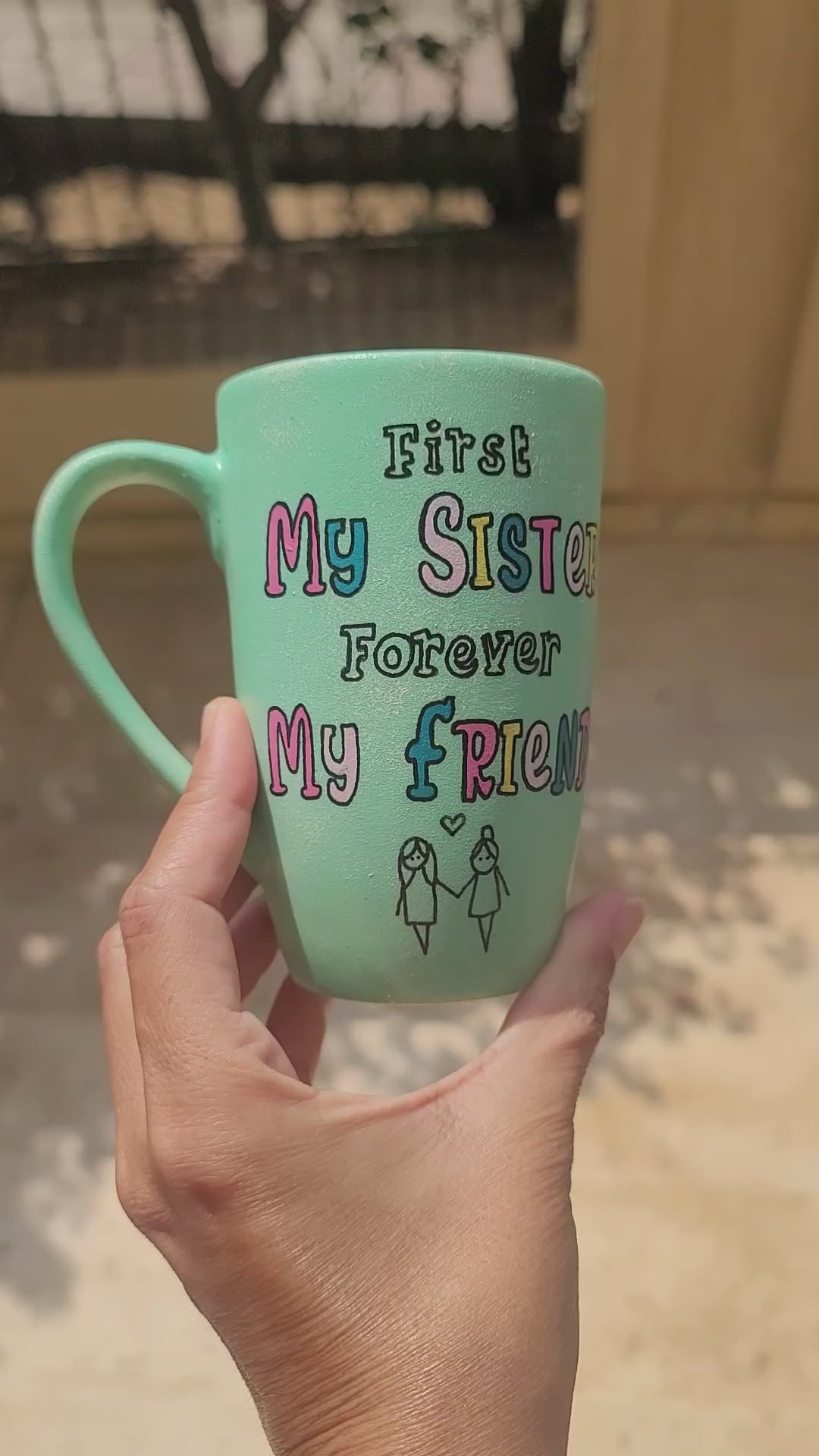 a mint green hand painted mug with the words "first my sister, forever my friend" and a sketch of 2 girl stick figures holding hands and the other side has the name Youstina