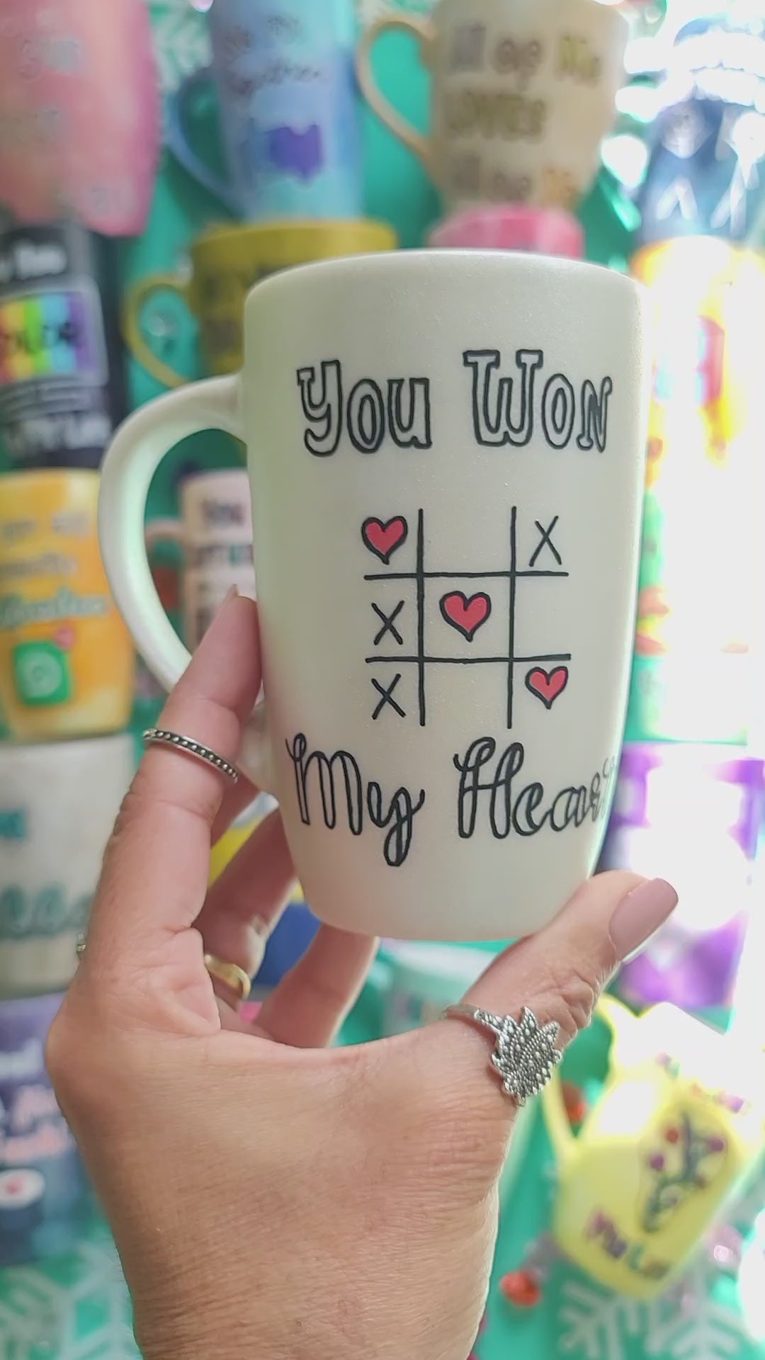 A hand painted pearl white mug with the sentence "you won" and under it an x o chart with hearts instead of o  and three hearts winning the game diagonally, then under it the words "My heart". then on the other side the name "Fayrouz"