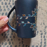 A Shimmery blue hand painted mug with a mandala split into 2 with a space in between that has the name 