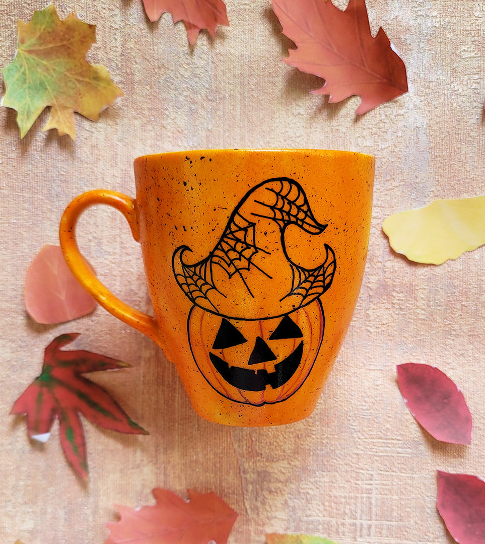 An Orange hand painted mug with black dots scattered all over and a pumpkin drawn on it