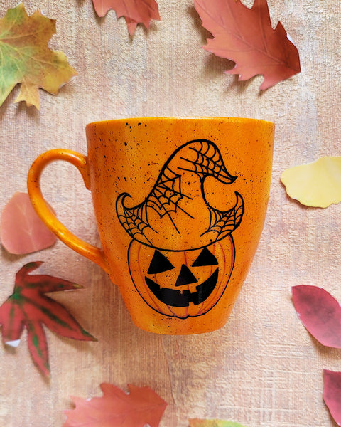 An Orange hand painted mug with black dots scattered all over and a pumpkin drawn on it