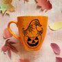 An Orange hand painted mug with black dots scattered all over and a pumpkin drawn on it