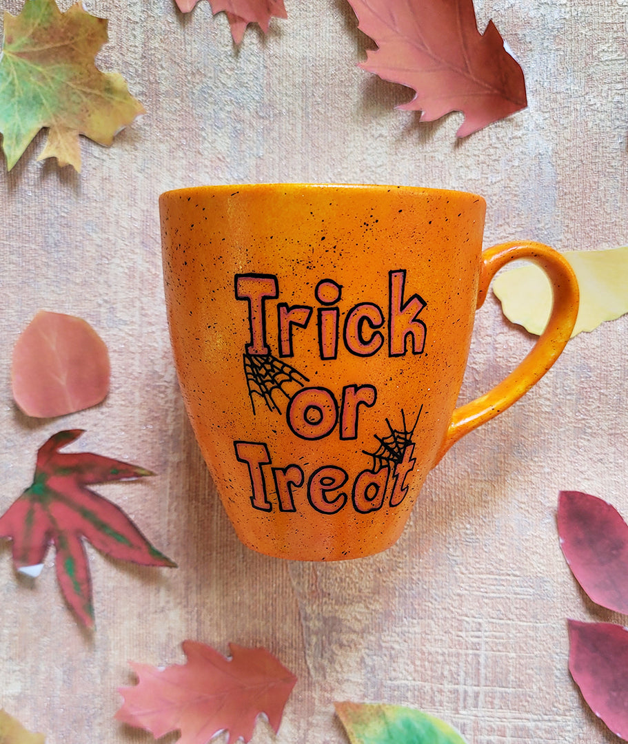 An Orange hand painted mug with black dots scattered all over and the words "trick or treat" written in black