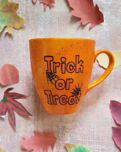 An Orange hand painted mug with black dots scattered all over and the words "trick or treat" written in black