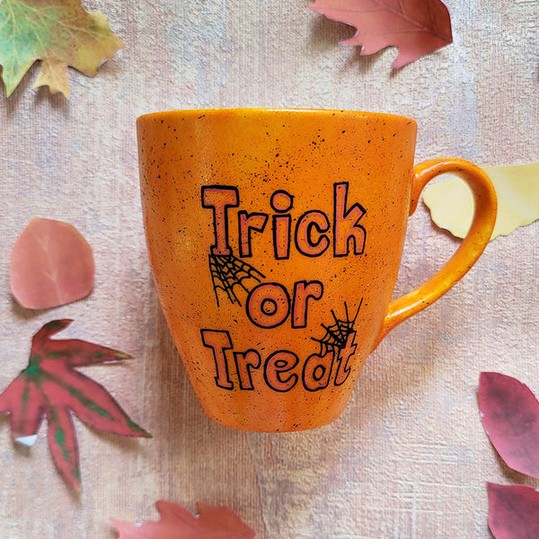 An Orange hand painted mug with black dots scattered all over and the words "trick or treat" written in black