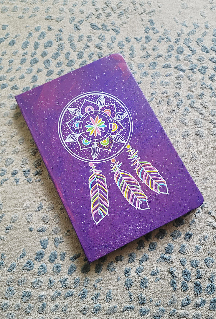 A Purple galaxy hand painted notebook with a dreamcatcher drawn in white