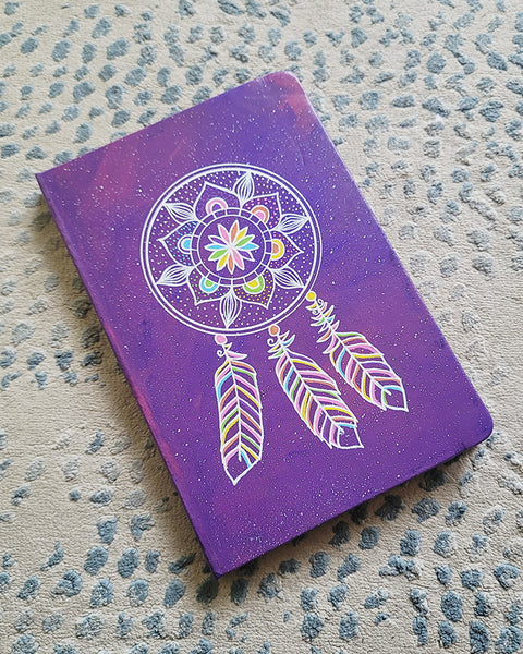 A Purple galaxy hand painted notebook with a dreamcatcher drawn in white