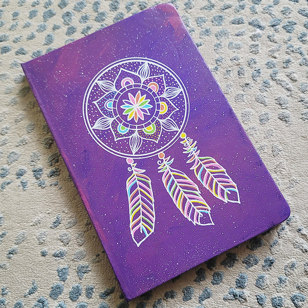 A Purple galaxy hand painted notebook with a dreamcatcher drawn in white