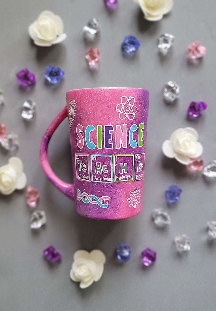 A Pink Galaxy Hand painted mug with the word Science on it and under it the word teacher written in the form of periodic table elements. with science items scattered all over