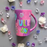 A Pink Galaxy hand painted mug with the name Julie written in the center and science items scattered al over 