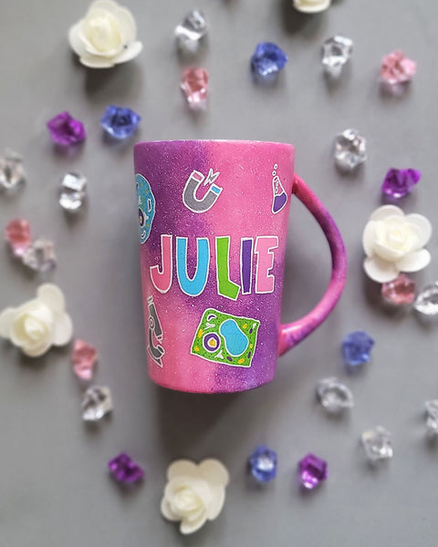 A Pink Galaxy hand painted mug with the name Julie written in the center and science items scattered al over "plant cell, animal cell, telescope, magnet....etc."