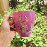 A Pink Galaxy Hand painted Mug With a Scorpio Design on it in white and outlines with purple