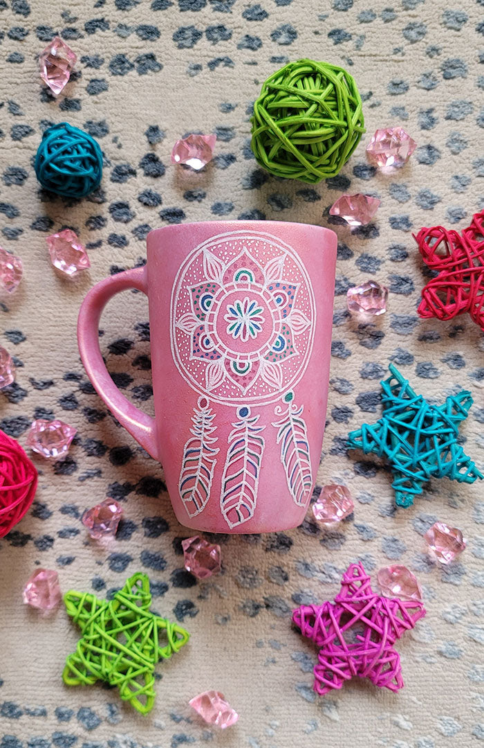 A Shimmery Pink hand painted mug with a dreamcatcher in white and colored in with (pink, blue and teal))