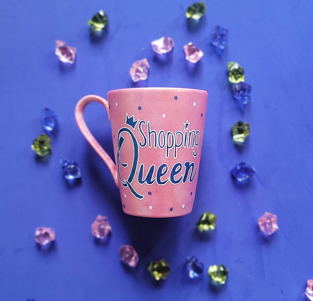 a shimmery pink hand paitned mug with teh words shopping queen written in white a shimmery blue. with blue and white dots scattered all over the mug